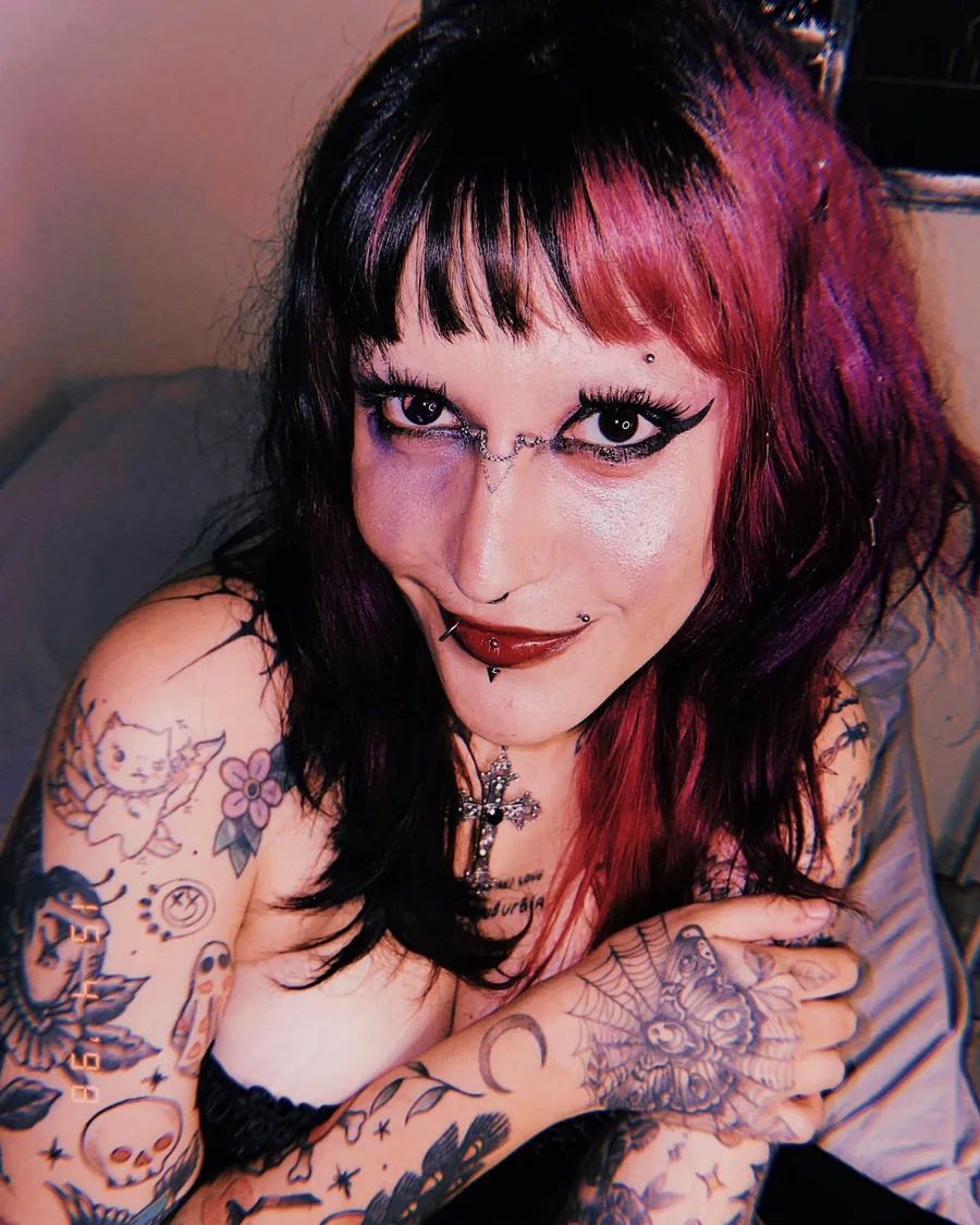 Tali Piercer sorrindo, com piercings no rosto e os braços tatuados